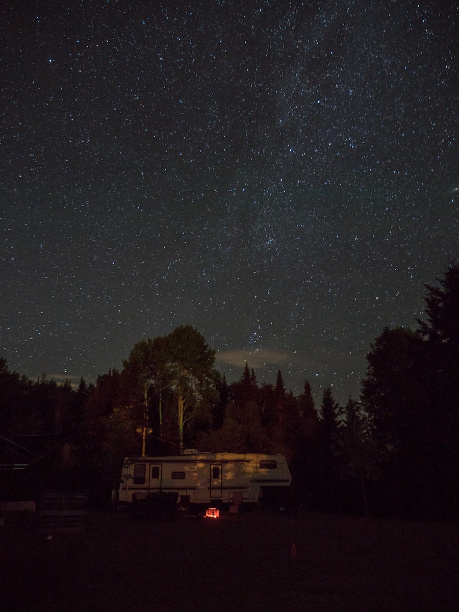 white RV trailer surrounded by trees during nighttime